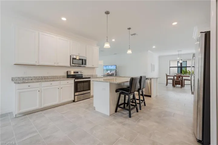 Kitchen with a kitchen breakfast bar, white cabinetry, light stone countertops, appliances with stainless steel finishes, and pendant lighting