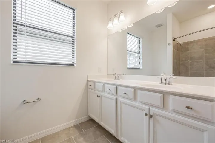 Bathroom with vanity with extensive cabinet space, dual sinks, and tile floors