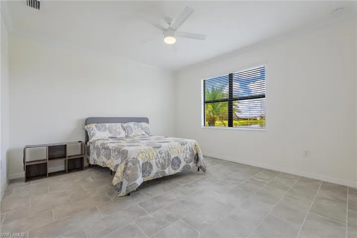 Bedroom with ceiling fan, light tile flooring, and ornamental molding