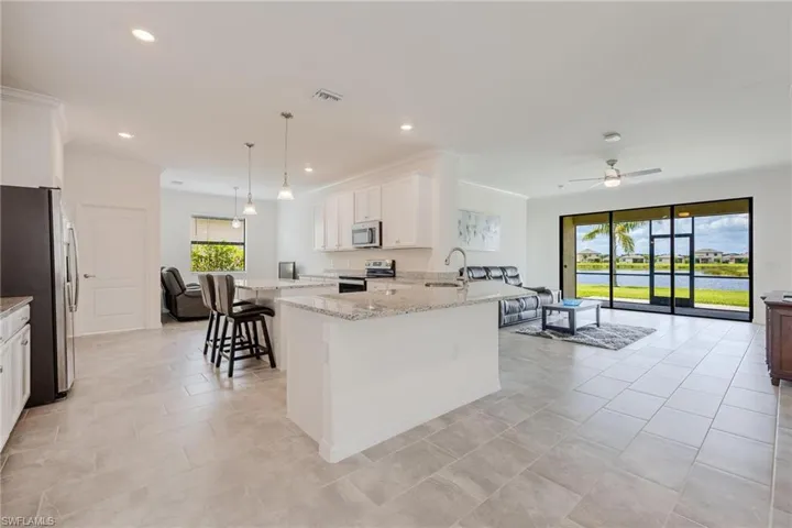 Kitchen with stainless steel appliances, light stone counters, pendant lighting, sink, and a kitchen bar