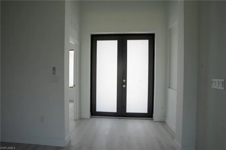 Double entry doors featuring frosted glass panels and dark frames, complemented by light wood-finish flooring