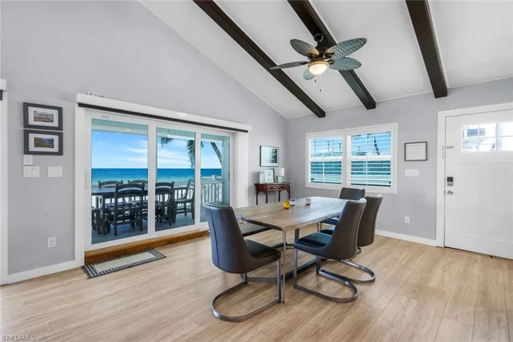 Dining area featuring light wood finished floors, beam ceiling, high vaulted ceiling, a water view, and ceiling fan