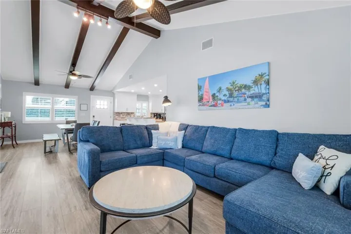 Living room with high vaulted ceiling, wood finished floors, beamed ceiling, and a ceiling fan