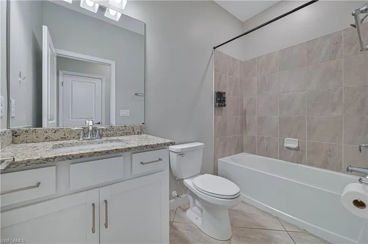 Bathroom featuring a white vanity cabinet with stone-finish countertop, undermount sink, large wall-mounted mirror, and tile surround tub-shower combo