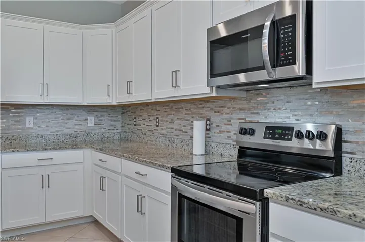 White cabinetry featuring stainless steel hardware, stone-finish countertops, tiled mosaic backsplash, and built-in stainless steel appliances