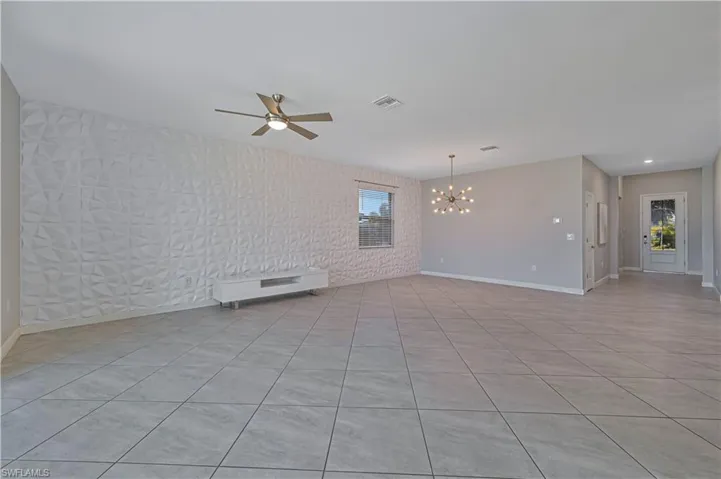 Open-concept interior featuring large-format tile flooring, a geometric textured accent wall, a central sputnik-style chandelier, and a brushed nickel ceiling fan