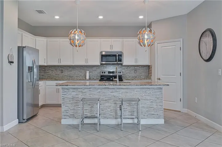 Kitchen featuring white cabinetry, stone countertops, stainless steel appliances, a center island with a tiled base, and mosaic tile backsplash