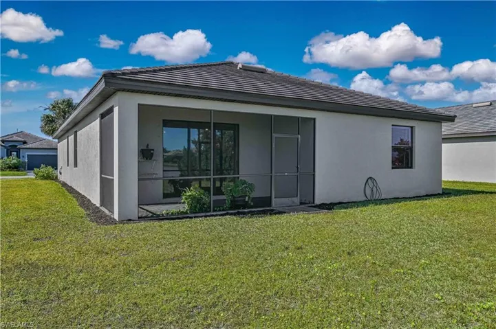 Rear exterior featuring a stucco facade, dark-toned hip roof, screened-in lanai, and open grass lawn
