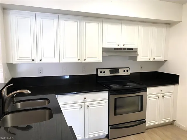 Kitchen with stainless steel electric stove, under cabinet range hood, white cabinetry, and dark countertops