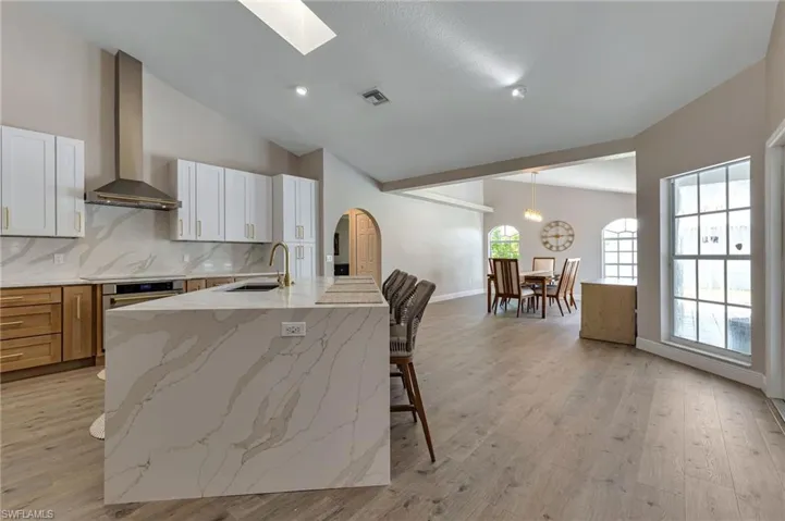 Kitchen with white cabinets, sink, light stone counters, oven, and wall chimney exhaust hood