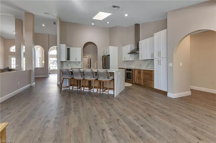 Kitchen with wall chimney range hood, white cabinetry, decorative backsplash, and a towering ceiling