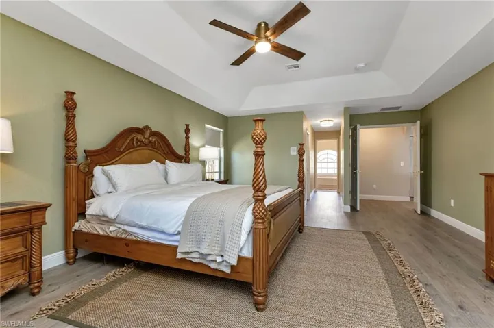 Bedroom featuring ceiling fan, a tray ceiling, and light hardwood / wood-style floors