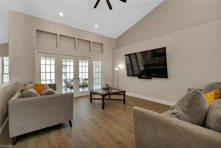 Living room with high vaulted ceiling, hardwood / wood-style flooring, french doors, and ceiling fan