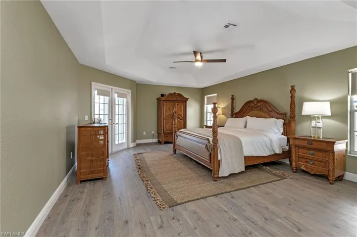 Bedroom featuring ceiling fan, light hardwood / wood-style floors, french doors, and a tray ceiling