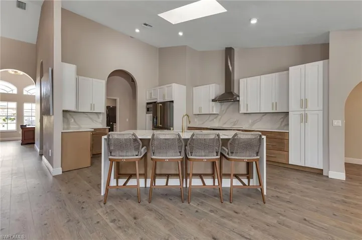 Kitchen with a skylight, high quality fridge, an island with sink, wall chimney exhaust hood, and decorative backsplash