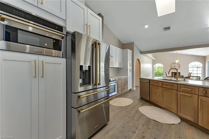 Kitchen with appliances with stainless steel finishes, light hardwood / wood-style flooring, white cabinets, tasteful backsplash, and sink