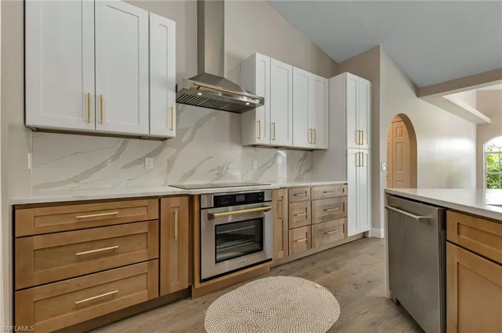 Kitchen featuring white cabinets, stainless steel appliances, light hardwood / wood-style floors, and wall chimney exhaust hood