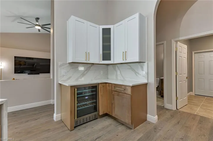 Kitchen featuring white cabinetry, tasteful backsplash, light wood-type flooring, beverage cooler, and ceiling fan