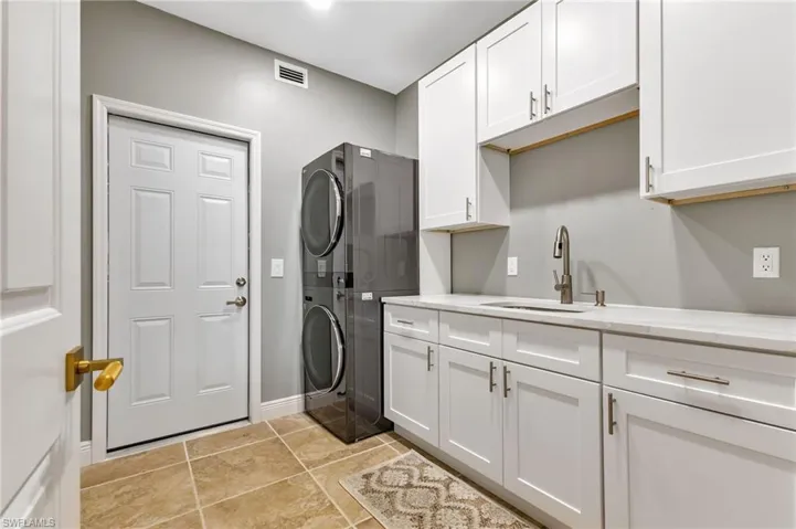 Laundry area featuring sink, cabinets, stacked washing maching and dryer, and light tile patterned floors