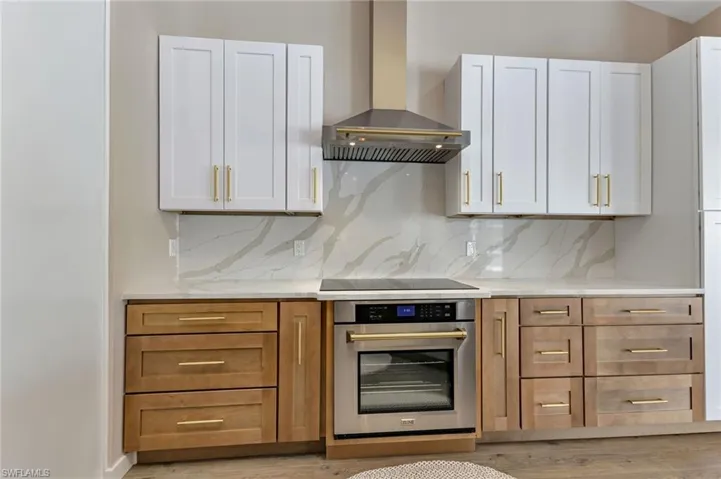 Kitchen with white cabinetry, tasteful backsplash, light wood-type flooring, wall chimney exhaust hood, and oven