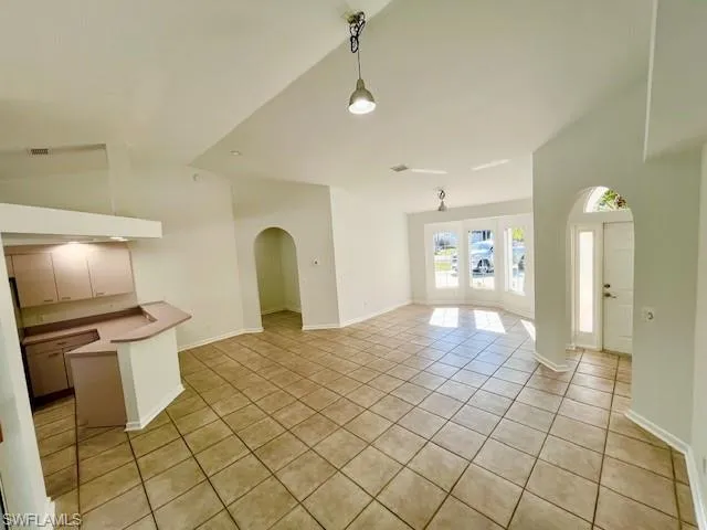 Unfurnished living room with arched walkways, light tile patterned floors, and vaulted ceiling