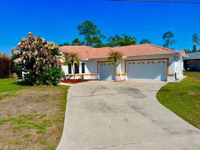View of front of home featuring an attached garage, a tile roof, concrete driveway, stucco siding, and a front lawn