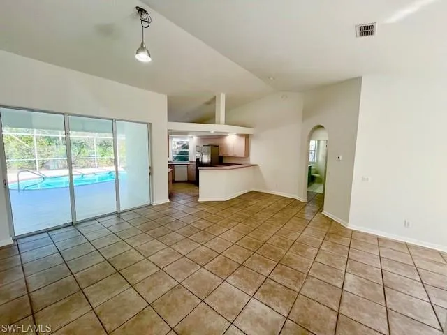 Unfurnished living room featuring arched walkways, lofted ceiling, and dark tile patterned floors