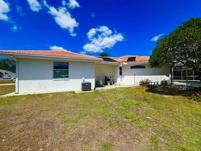 Back of property featuring a tiled roof, a yard, glass enclosure, and stucco siding