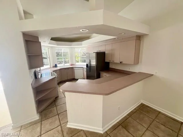 Kitchen with a peninsula, open shelves, a raised ceiling, white dishwasher, and stainless steel fridge with ice dispenser