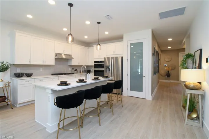 Kitchen with white cabinetry, stainless steel appliances, decorative light fixtures, an island with sink, and a kitchen breakfast bar