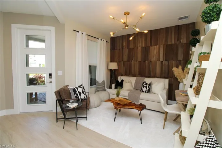 Living area with light wood-style flooring, wood walls, suspended lighting, an accent wall, and a high ceiling