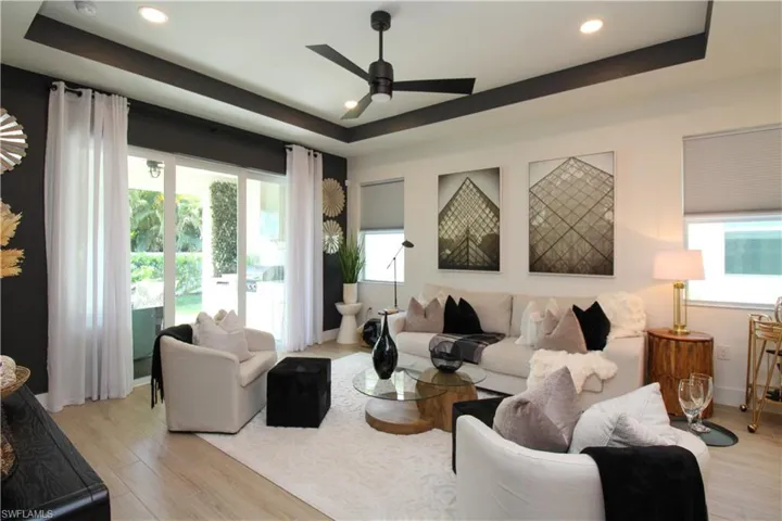 Living area featuring a raised ceiling, ceiling fan, light wood-style floors, and recessed lighting