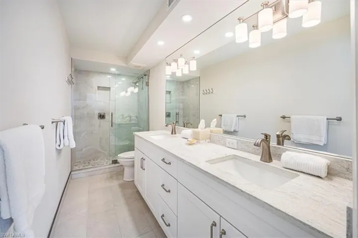 Primary bathroom features a double sink vanity, tile flooring and a shower with a frameless shower door
