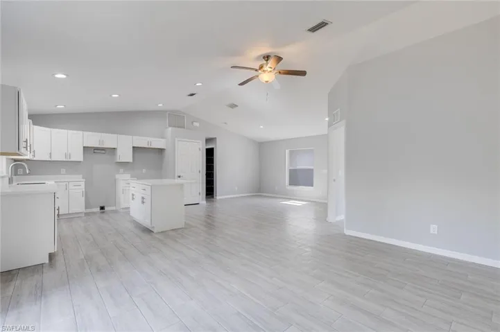 Kitchen with a center island, light wood finished floors, white cabinets, ceiling fan, and lofted ceiling