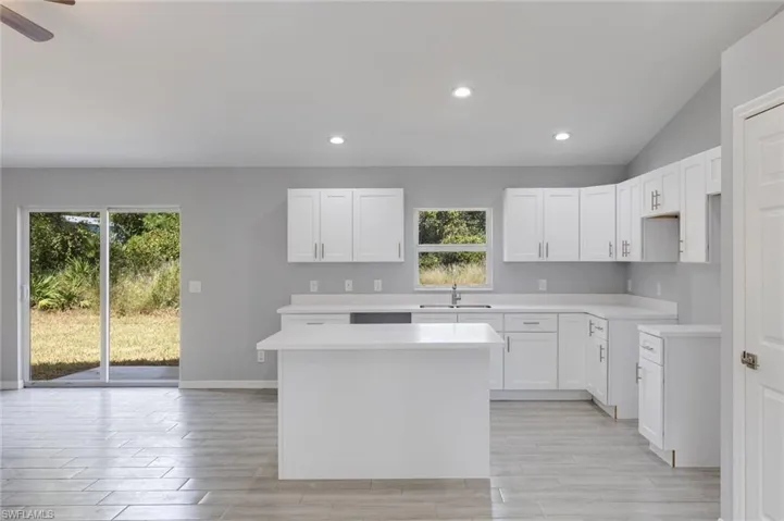 Kitchen featuring white cabinetry, recessed lighting, wood finish floors, a center island, and vaulted ceiling