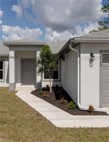 Entrance to property featuring a yard, stucco siding, and roof with shingles