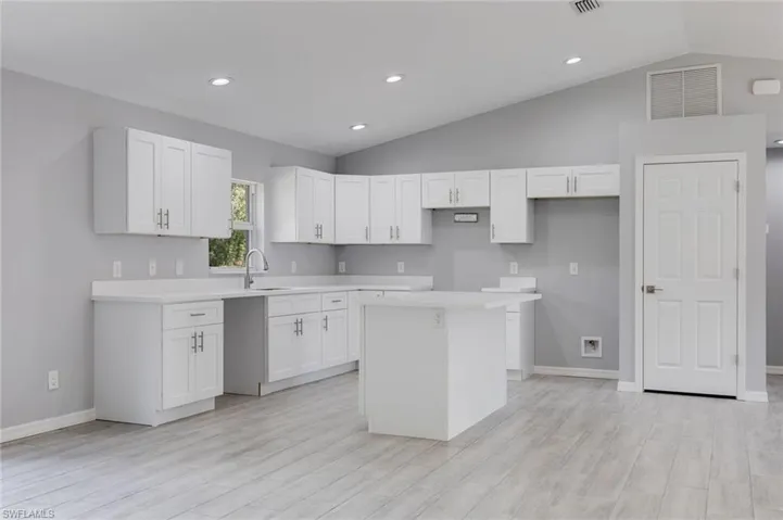 Kitchen featuring white cabinetry, vaulted ceiling, light wood-style floors, a center island, and recessed lighting