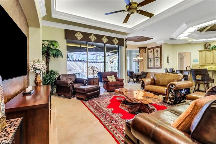 Living room featuring light tile patterned floors, a tray ceiling, and crown molding looks out to large courtyard pool and lanai!
