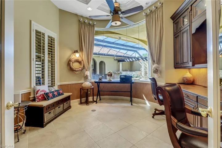 Home office with a wainscoted wall, built-in desk, and unique ceiling fan overlooking lanai