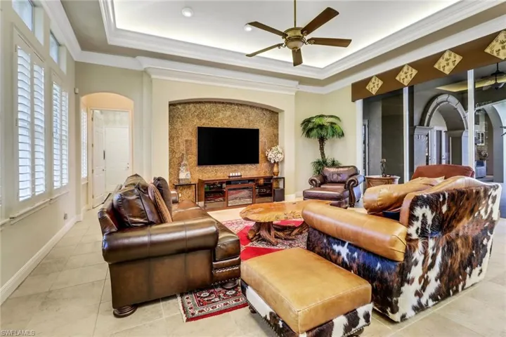 Living room featuring arched walkways, a raised ceiling, and crown molding