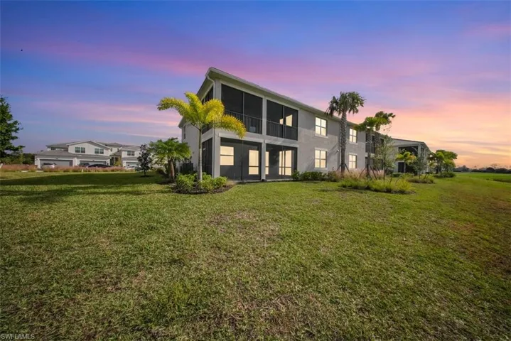 Back of property at dusk featuring a sunroom, a yard, and stucco siding