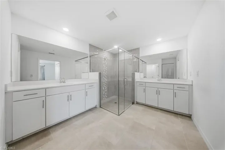 Bathroom featuring two vanities, a stall shower, recessed lighting, and light tile patterned flooring