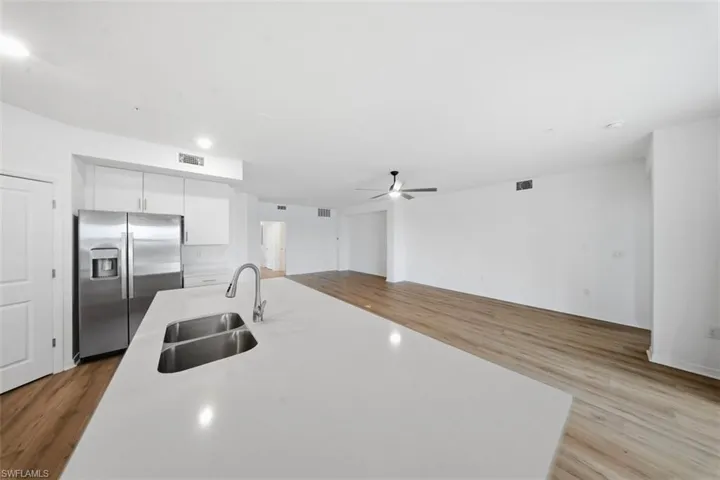 Kitchen featuring stainless steel refrigerator with ice dispenser, light wood finished floors, white cabinets, and open floor plan