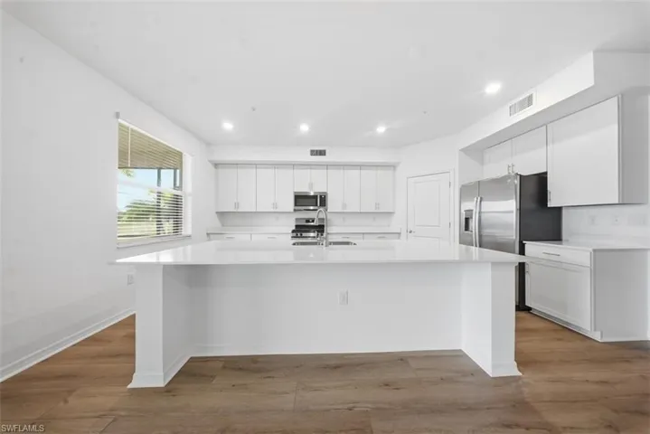 Kitchen featuring white cabinetry, a spacious island, recessed lighting, light wood-style floors, and light stone countertops