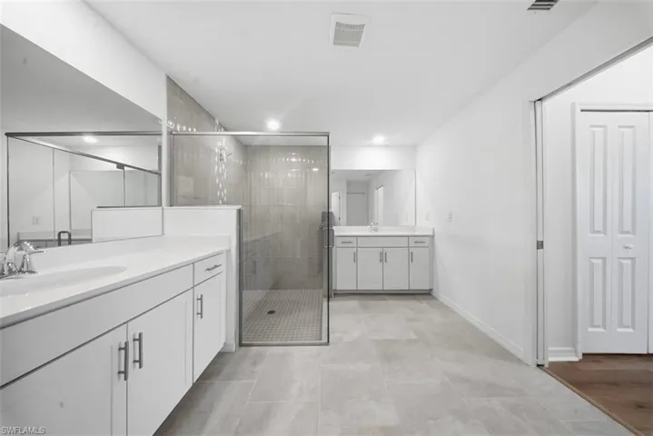 Bathroom with two vanities, a stall shower, recessed lighting, and light tile patterned floors