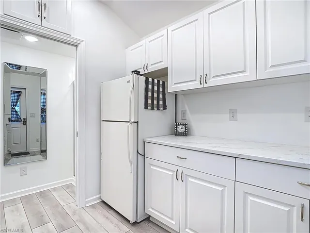 Kitchen featuring white cabinetry, light stone countertops, wood finish floors, and freestanding refrigerator