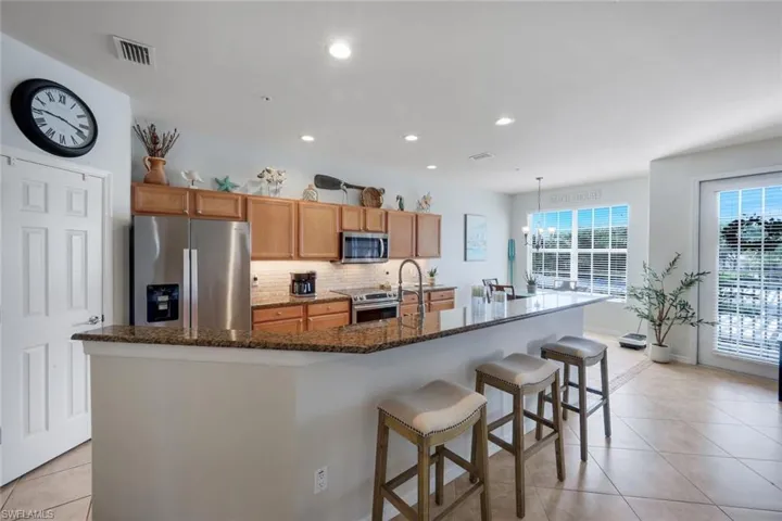 Open-concept kitchen featuring an expansive breakfast bar, recessed lighting, tile flooring, stainless steel appliances, and wood cabinetry