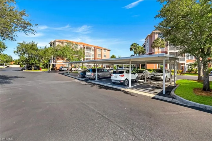 Paved parking area with covered carports, landscaping, and multi-story residential buildings