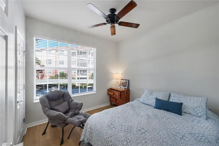 Spacious room featuring wood-finish flooring, a ceiling fan with integrated lighting, and a large window with horizontal blinds