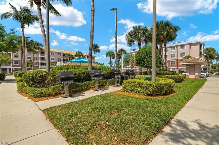 Outdoor grilling station featuring multiple built-in grills, bordered by manicured shrubbery and green lawn